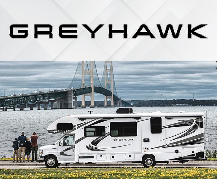 Photo of family standing beside Jayco Greyhawk class C motorhome with bridge in background and logo above.