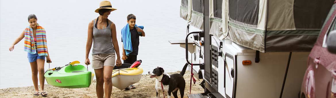 Family kayaking at lake with popup camper in foreground.